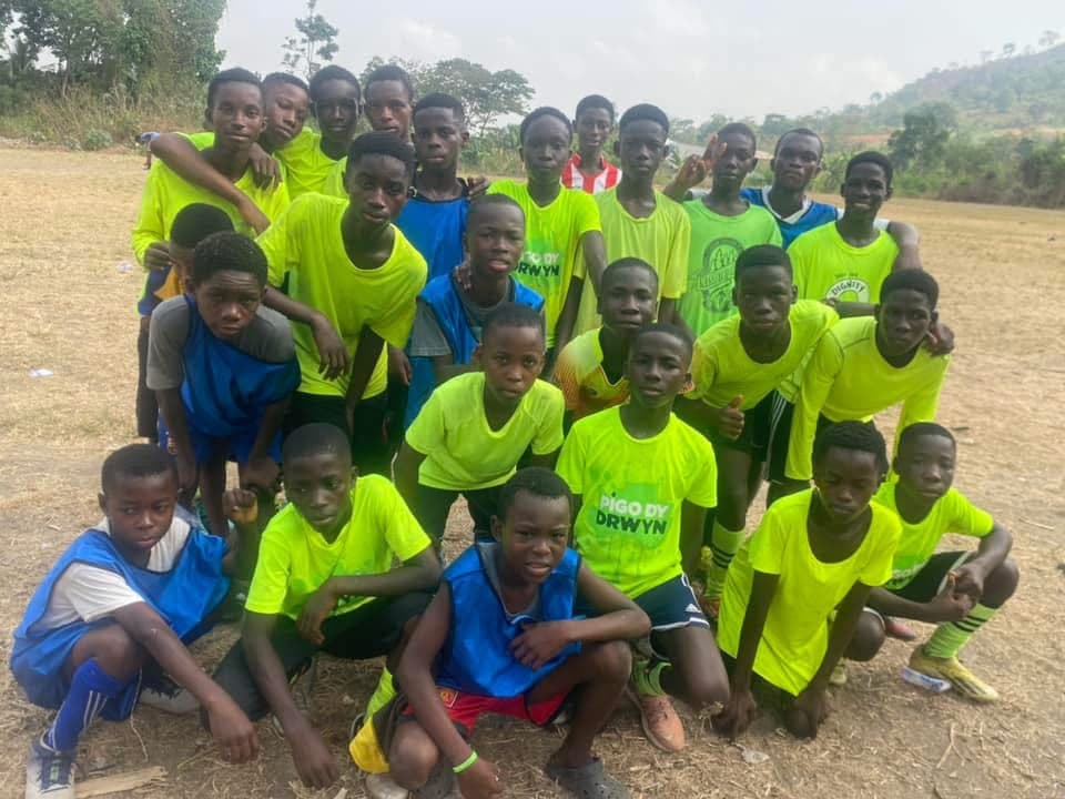 A group of young players in bright green and blue bibs posing together on a dirt pitch