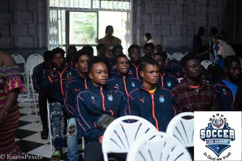 Players in navy academy tracksuits seated in rows indoors during an academy event