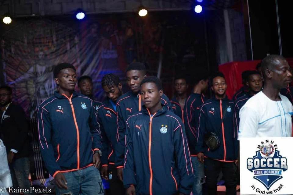 Players in navy academy tracksuits standing on a lit stage during an indoor event