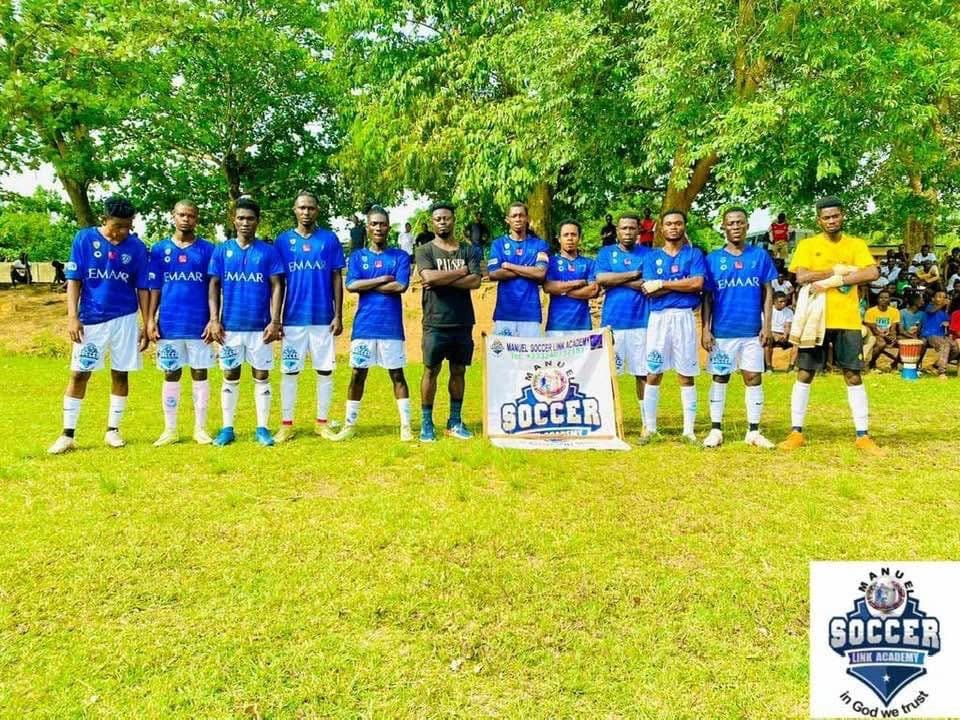 Players in blue kit standing with an academy banner in front of a crowd on a grass pitch