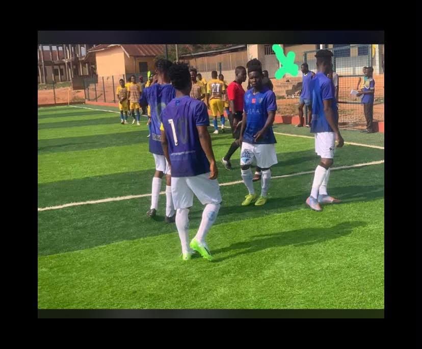 Players in blue kit walking across a turf pitch during a match against a team in yellow