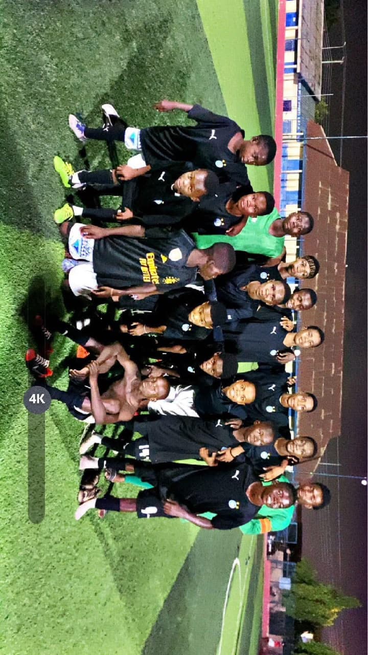 Players in black kit posing together for a group photo pitchside at night